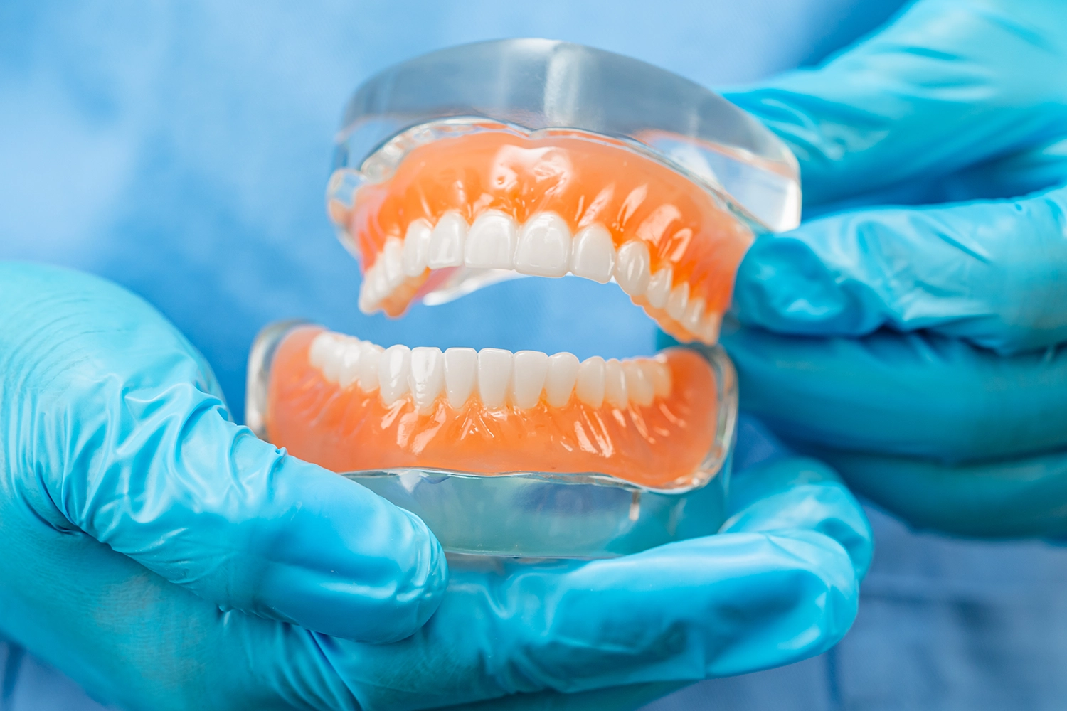 Complete upper and lower denture set displayed in gloved hands